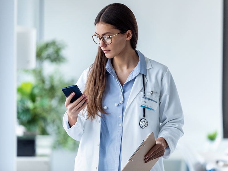 doctor using her mobile phone while standing in medical office